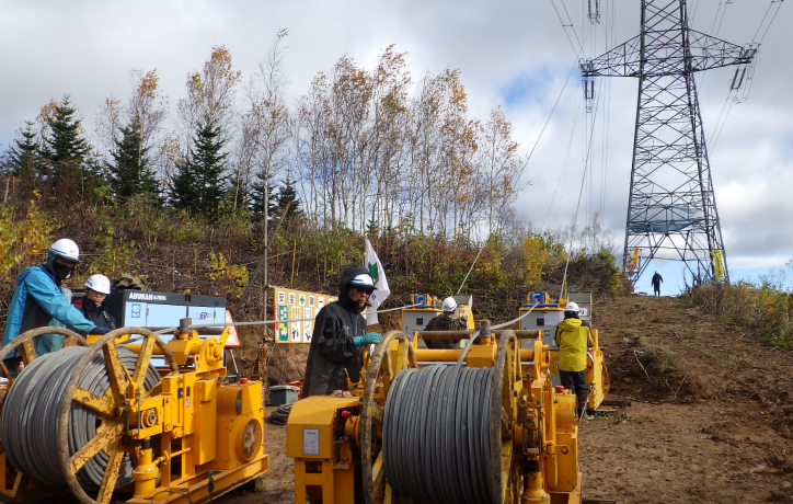 電線延線作業の様子、電線を鉄塔へと送り出し、張力の調整を行う